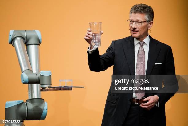 Dpatop - 27 April 2018, Germany, Hannover: Elmar Degenhart, CEO of Continental AG, showing a glass half-filled with water next to a Cobot robot,...