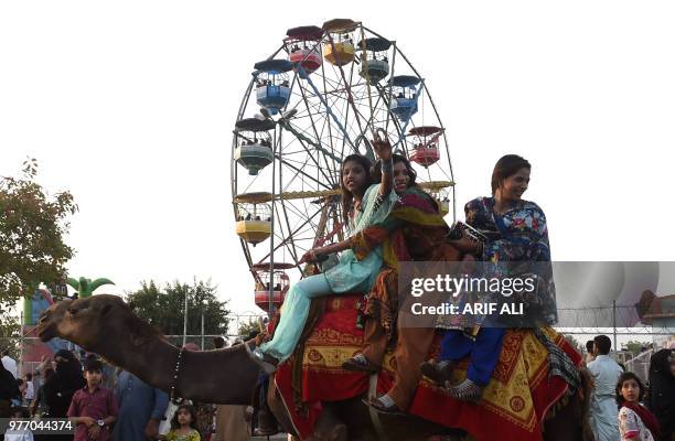 Pakistani girls ride on a camel on the second day of Eid al-Fitr celebration in Lahore on June 17, 2018. - Muslims around the world celebrated Eid al...