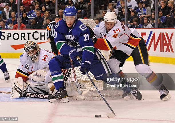 Goalie Vesa Toskala of the Calgary Flames keeps an eye on Mason Raymond of the Vancouver Canucks as he comes from behind the net while being checked...