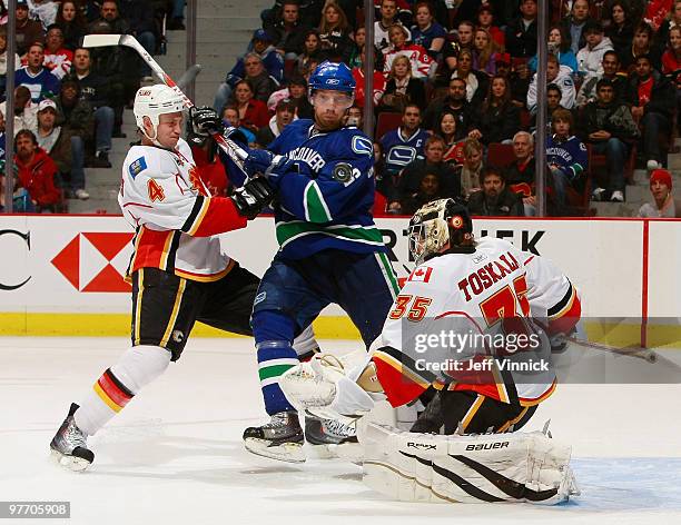 Mikael Samuelsson of the Vancouver Canucks and Jay Bouwmeester of the Calgary Flames check one another in front of Vesa Toskala during their game at...