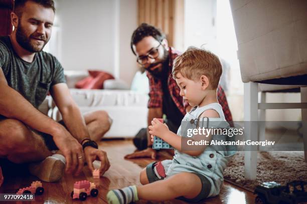 pareja gay jugando con el hijo adoptado de bebé y sus juguetes - gay fotografías e imágenes de stock