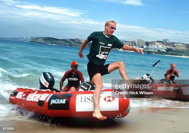 Eddie Irvine of Northern Ireland jumps from a IRB rescue boat onto Bondi Beach, Sydney during some races with JaguarF1 teammate Luciano Burti of...