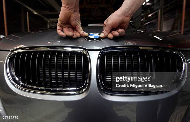 Man attaches the BMW logo onto the hood of a car on the BMW 3-series production line at the BMW factory on March 15, 2010 in Munich, Germany. The...