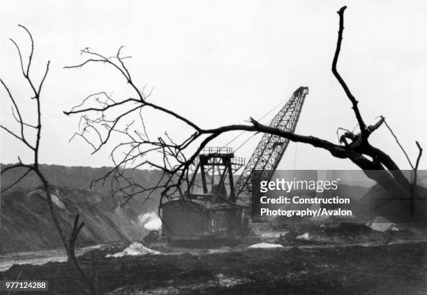 The woodlands retreat as the dragline moves across the workings at Nassington Ironstone Mine in the late 1960s. Poles of Silica white sand - a...