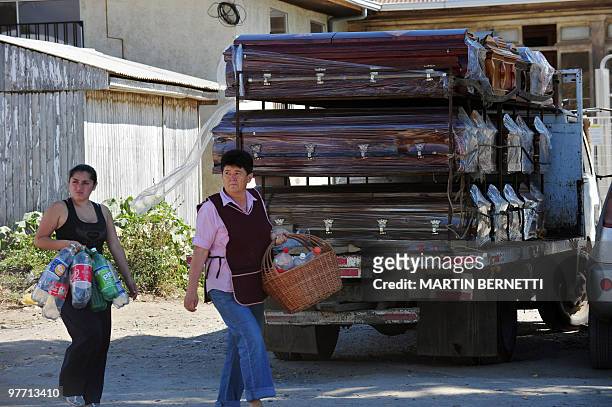 Women pass in front of a truck with coffins as they go to get water after the arrival of supplies on March 2, 2010 in the fishing village of...
