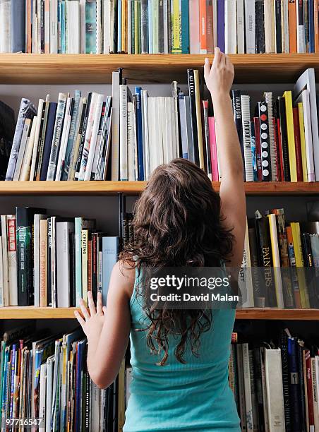 young woman reaching for a book on a bookshelf - ärmelloses oberteil stock-fotos und bilder