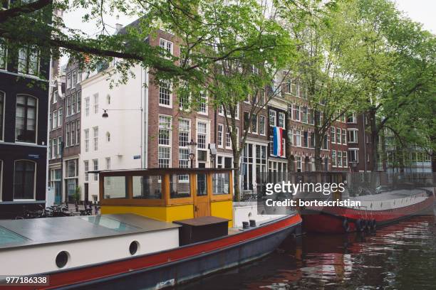 boats moored in canal by buildings in city - bortes stockfoto's en -beelden