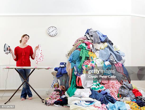 woman ironing next to very large pile of clothes - dirty clothes stock pictures, royalty-free photos & images