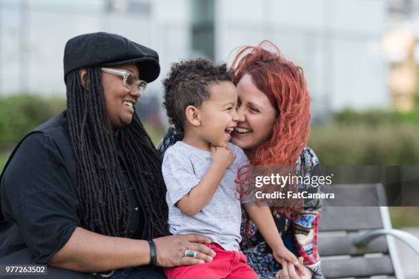 twee moeders houden van hun zoon op hun rondjes buiten in het park - lesbian stockfoto's en -beelden
