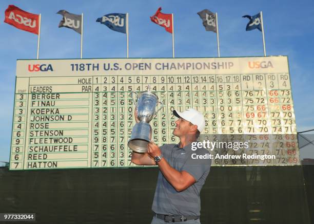 Brooks Koepka of the United States celebrates with the U.S. Open Championship trophy in front of the final leaderboard after winning the 2018 U.S....