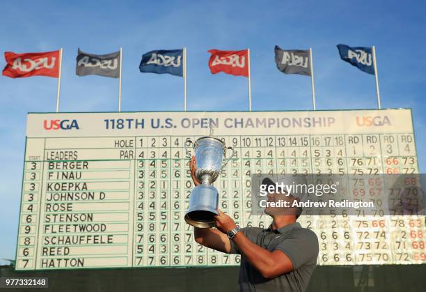 Brooks Koepka of the United States celebrates with the U.S. Open Championship trophy in front of the final leaderboard after winning the 2018 U.S....