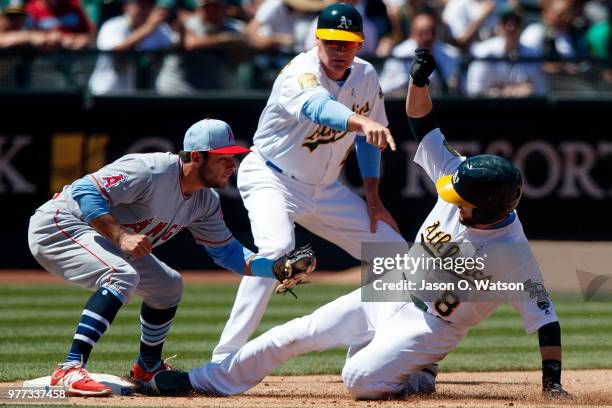 Jed Lowrie of the Oakland Athletics slides into third base ahead of a tag from David Fletcher of the Los Angeles Angels of Anaheim in front of third...
