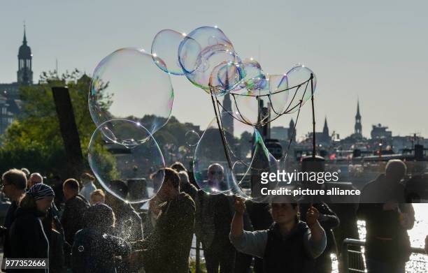 May 2018, Germany, Hamburg: Soap bubbles glitter in the sun above people at the Fischmarkt. Photo: Axel Heimken/dpa