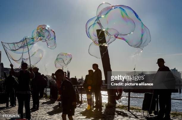 May 2018, Germany, Hamburg: Soap bubbles glitter in the sun above people at the Fischmarkt. Photo: Axel Heimken/dpa