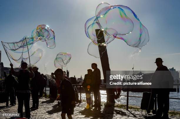 Soap bubbles glitter in the sun above people at the Fischmarkt, in Hamburg, Germany, 06 May 2018. Photo: Axel Heimken/dpa