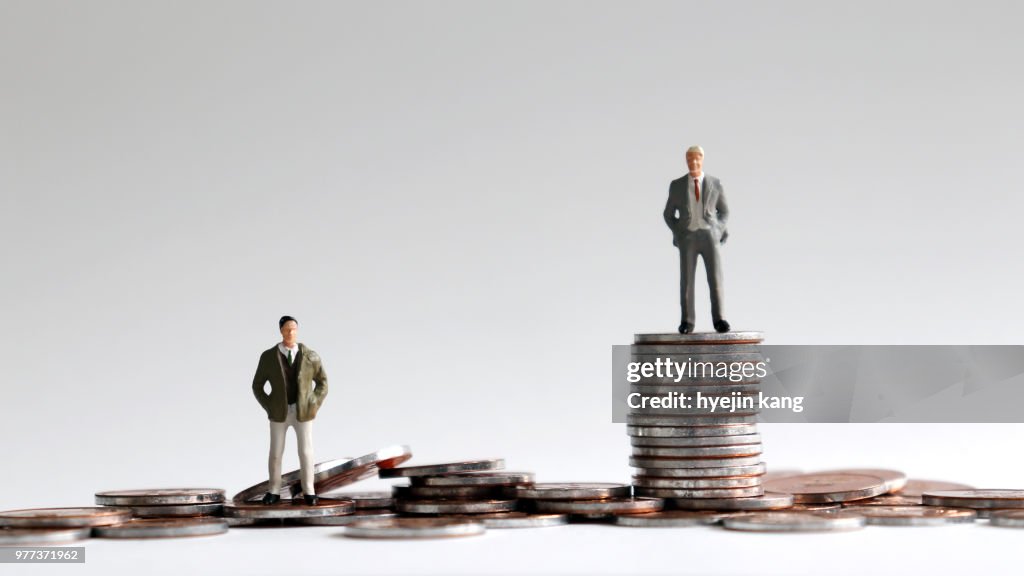 Gente miniatura de pie sobre una pila de monedas.