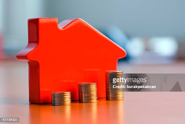 red 3d house model next to growing stacks of coins - playhouse stockfoto's en -beelden