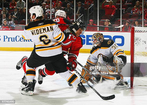 Dainius Zubrus of the New Jersey Devils is knocked off his feet into Dennis Wideman of the Boston Bruins look as goaltender Tim Thomas defends at the...