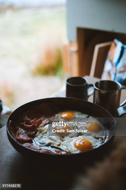 cooking eggs and bacon in skillet at campsite - camping stove stockfoto's en -beelden