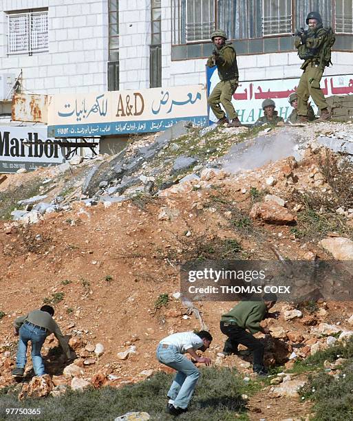Palestinian youths duck as Israeli soldiers prepare to fire 08 February 2002 in the West Bank town of Ramallah, during stone-throwing clashes with...