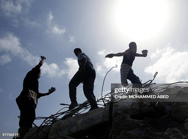 Palestinian youths, standing on the rubble of houses demolished by the Israeli army, throw stones at an Israeli checkpoint near the Jewish settlement...