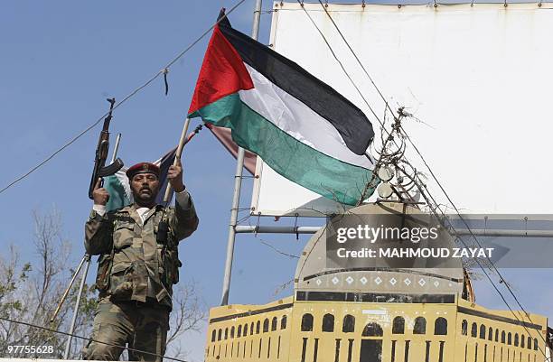 An armed Palestinian militant holds a national flag in front of a huge model of Jerusalem's Dome of the Rock mosque during a protest by Palestinian...