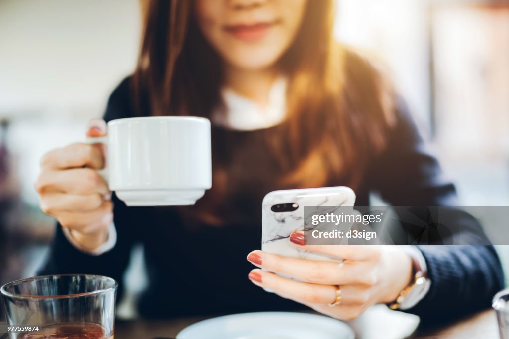 Close up of young woman having coffee and reading news on mobile phone in the early morning before work