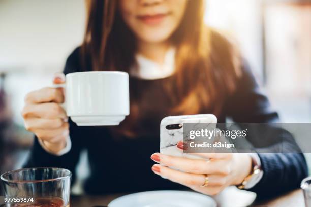 close up of young woman having coffee and reading news on mobile phone in the early morning before work - mobile apps stockfoto's en -beelden