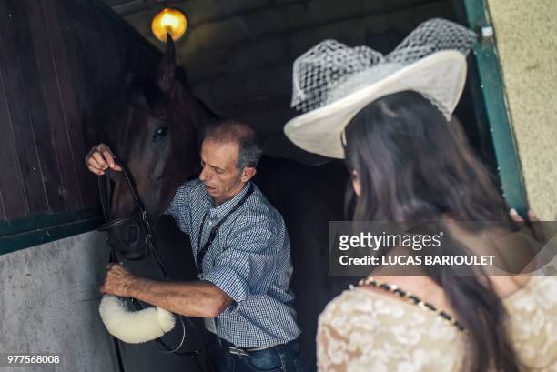 Woman wearing a hat watches as he man gets a horse ready for the 169th Prix de Diane horse racing on June 17, 2018 in Chantilly, northern Paris.