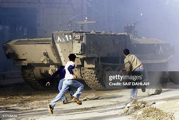 Palestinian children throw stones at an Israeli armored vehicle in the northern West Bank city of Jenin 12 December 2003. An Israeli armored column...