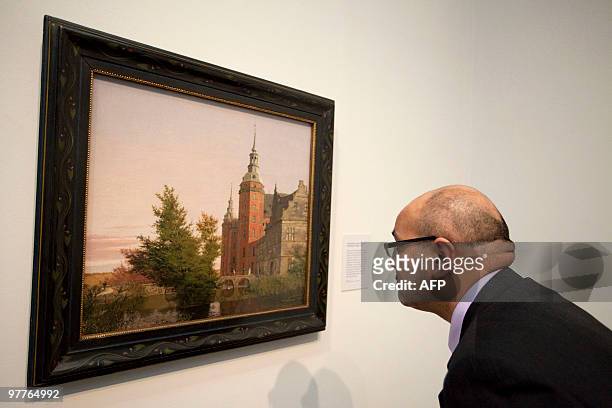 Gallery employee looks at a painting entitled 'Frederiksborg Castle,View near the Montbro Bridge' by Danish artist Christen Kobke during a press view...