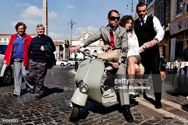 Pedestrians pass actors on a Piaggio Vespa motor scooter shooting an advertisement for German television near Piazza del Popolo in Rome, Italy, on...
