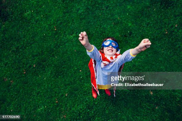 girl wearing a superhero costume standing in the garden with her arms in the air - helden stock-fotos und bilder