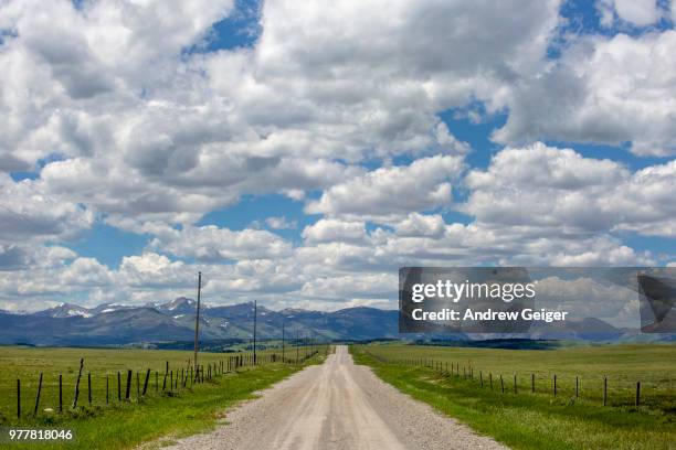 pov of rural gravel road and fence with rocky mountains and dramatic cloud filled sky in background. - rocky road stock pictures, royalty-free photos & images