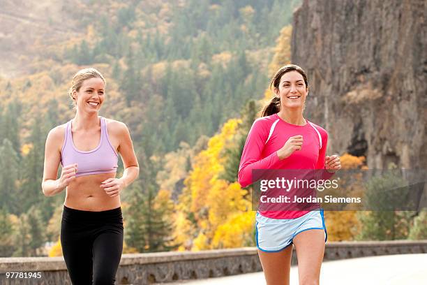 two females smile while jogging in the columbia gorge, oregon. bright colored fall trees illuminate  - bright smile stock-fotos und bilder