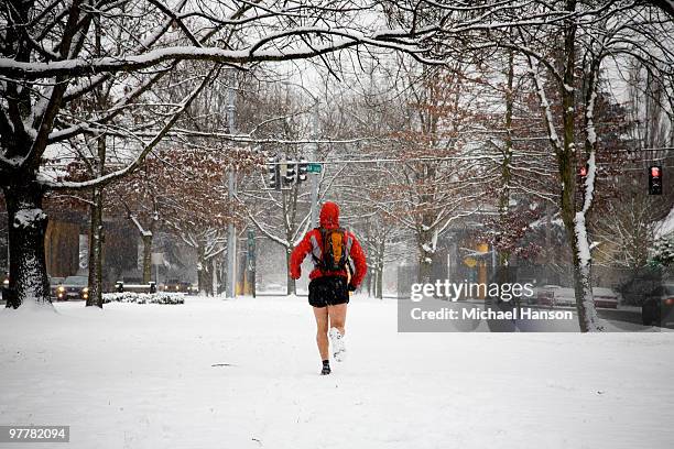 a male runner with a backpack runs down a city street while wearing shorts in the winter. - running shorts foto e immagini stock
