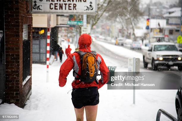 a male runner with a backpack runs down a city street while wearing shorts in the winter. - running shorts foto e immagini stock