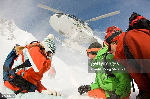 a group of skiers watch as their helicopter takes off from the drop zone in the selkirk mountains, c - heli skiing stock pictures, royalty-free photos & images