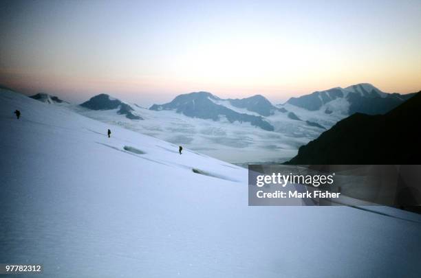 distant climbers cross a glacier in the chugach mountains of alaska at sunset. - foresta nazionale di chugach foto e immagini stock