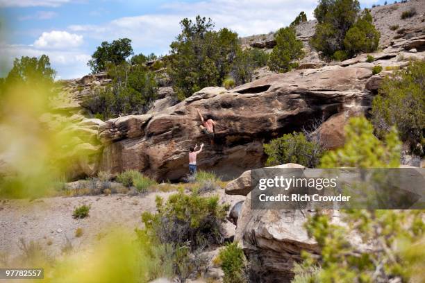 one man spots another while he climbs a bouldering problem in the triassic area, utah. - triassic landscape stock pictures, royalty-free photos & images