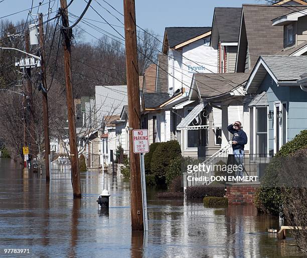 Man stands on the porch of his home on a street filled with floodewaters from the Passaic River on March 16, 2010 in Little Falls, New Jersey. Many...