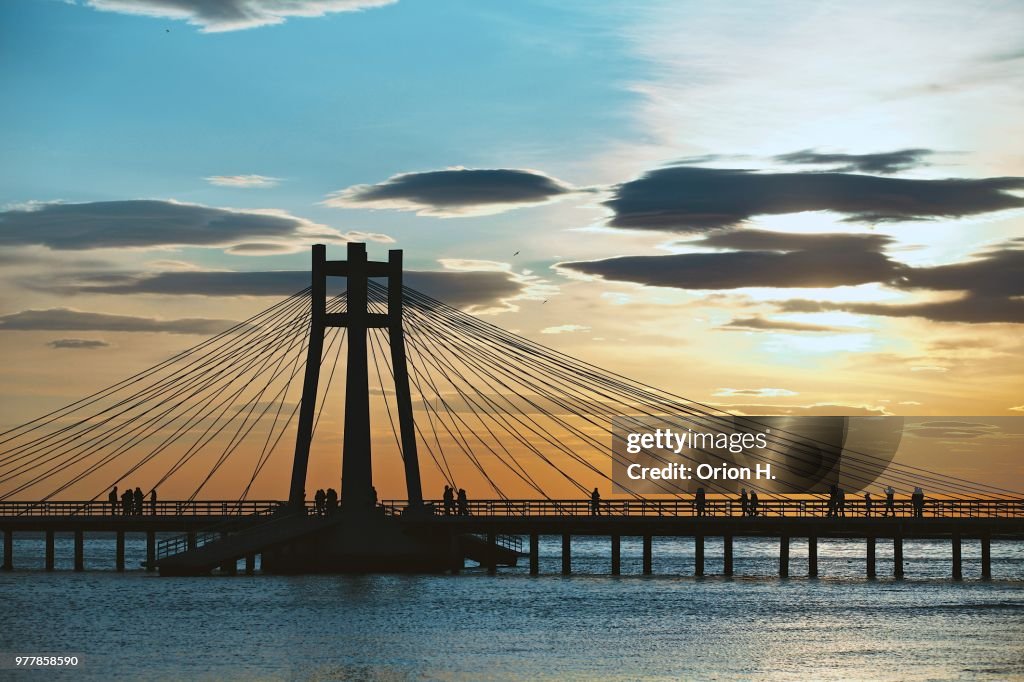 Silhouettes of people walking across bridge at sunset, Durres, Albania