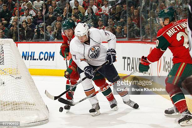 Tom Gilbert of the Edmonton Oilers handles the puck while being defended by Andrew Brunette and Antti Miettinen of the Minnesota Wild during the game...