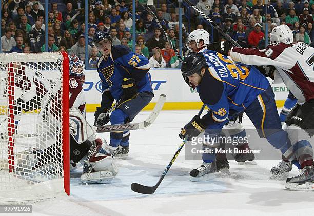 Carlo Colaiacovo of the St. Louis Blues takes a shove from T.J. Galiardi of the Colorado Avalanche in front of goaltender Peter Budaj on March 16,...