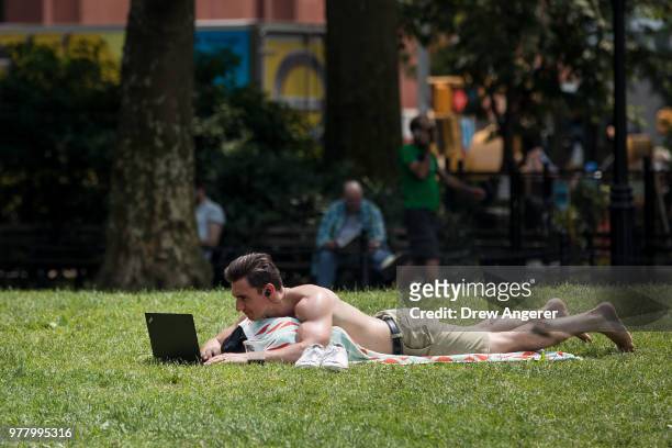 Man works on his laptop while laying out in Washington Square Park, June 18, 2018 in New York City. Temperatures are forecasted to hit the low 90s on...