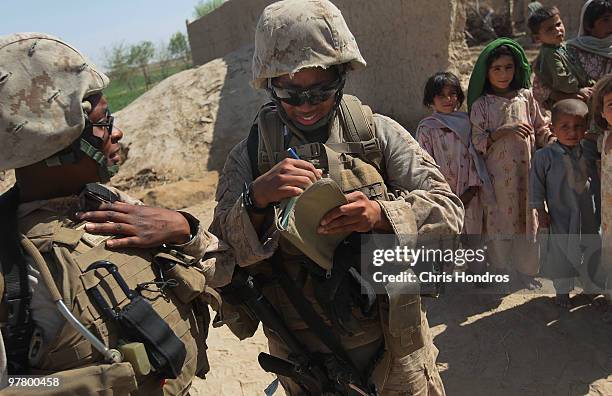 Marine Cpl. Ernstar Coriolan of Brooklyn, New York and Cpl. Ramona Brown of Fayetteville, North Carolina look over notes while young Pashtun girls...
