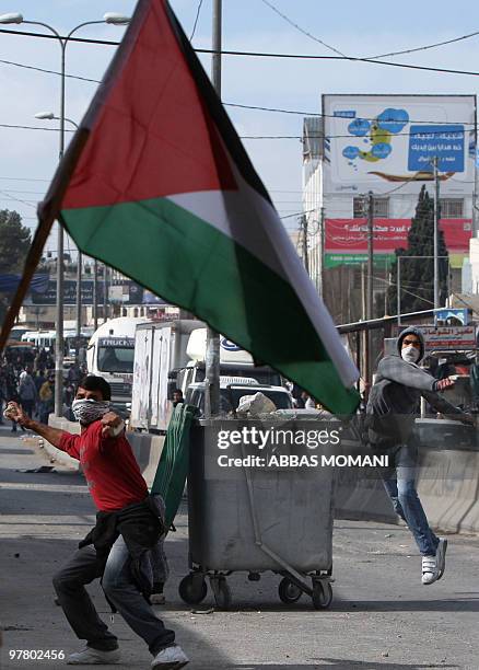 Palestinian flag flutters as protesters throw stones at Israeli troops during clashes on March 17, 2010 in the West Bank refugee camp of Qalandia....