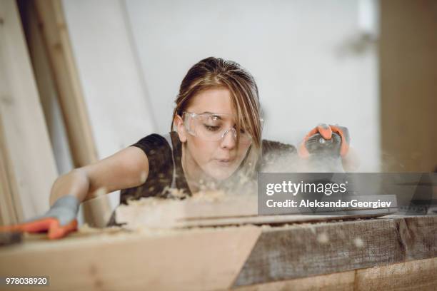 vrouwelijke carpenter blazen van stof tijdens het schuren de plank - carpenter stockfoto's en -beelden