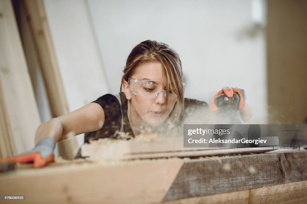 Female Carpenter Blowing Dust While Sanding Plank