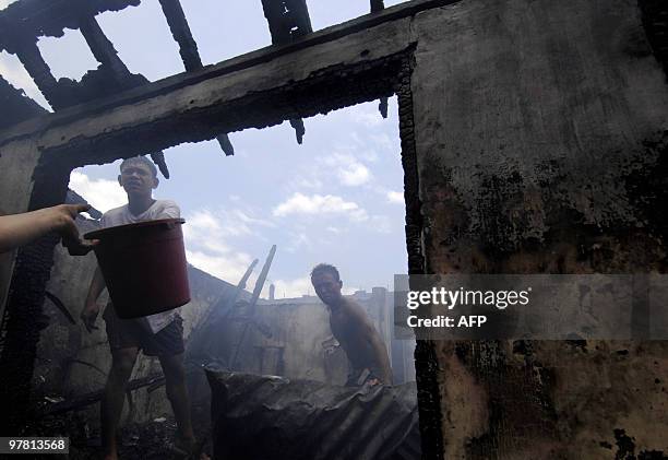 Residents pour water into a gutted house after a fire raced through a squatter area in Manila on March 18, 2010. Around 200 hundred houses were...